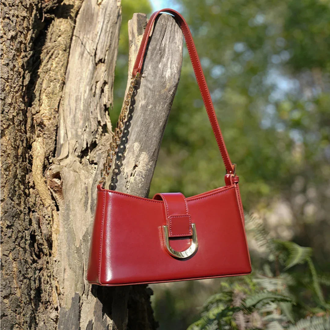 Red leather shoulder bag with gold buckle and chain on tree outdoors