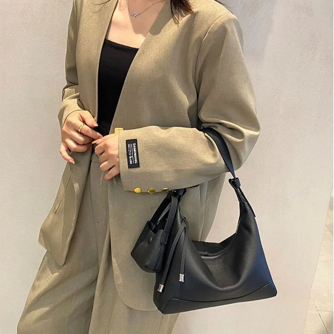 Woman in beige suit with black top holding a black leather shoulder bag