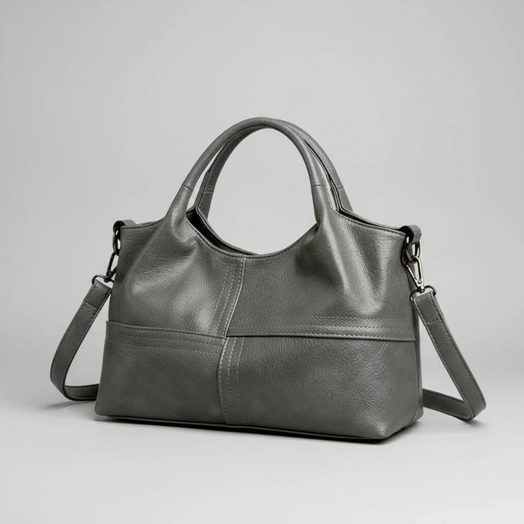 Gray leather handbag with short handles and detachable shoulder strap on plain background