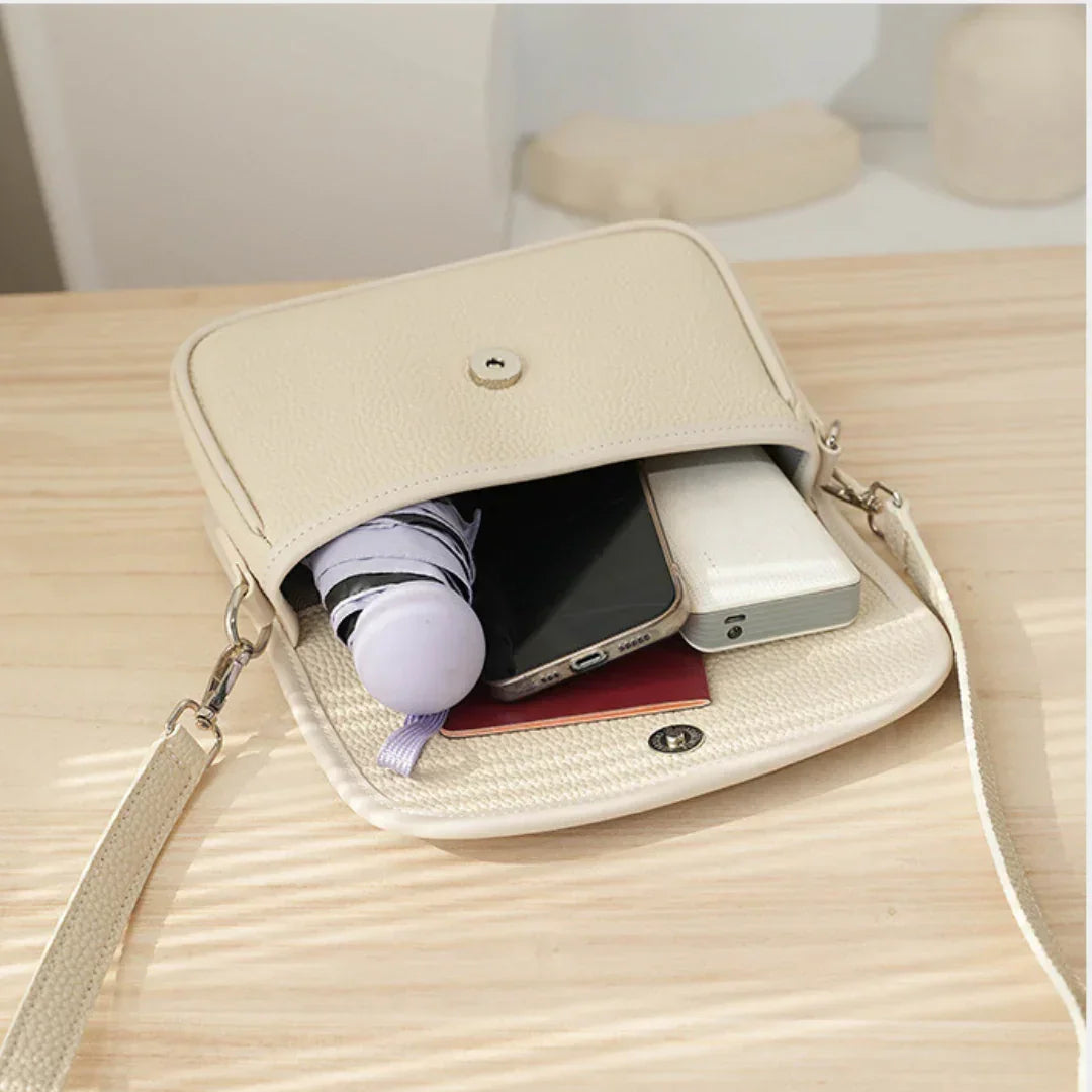 Beige crossbody bag with umbrella, smartphone, and power bank on light wood table