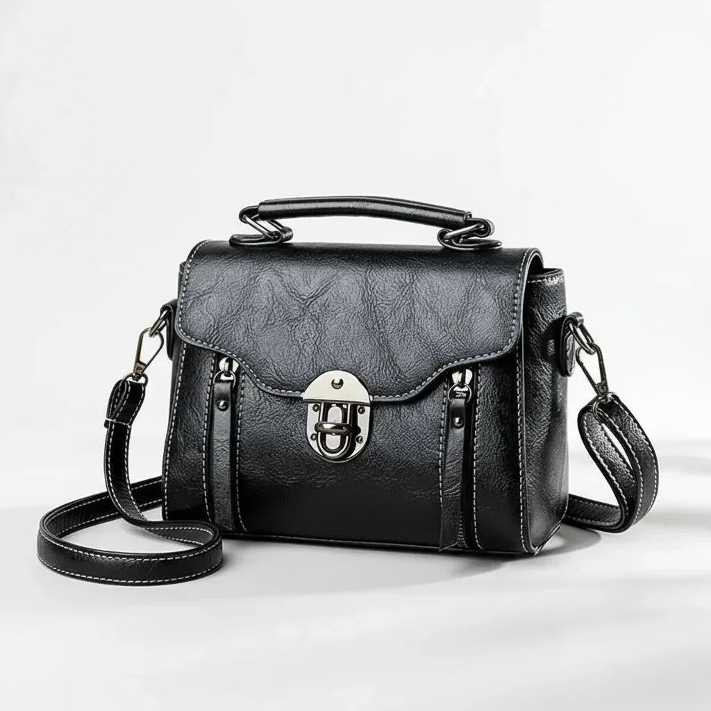 Black leather crossbody satchel bag with silver buckle and top handle on white background