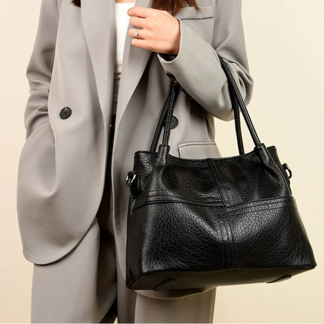 Woman in gray blazer holding a black leather tote handbag, stylish fashion accessory