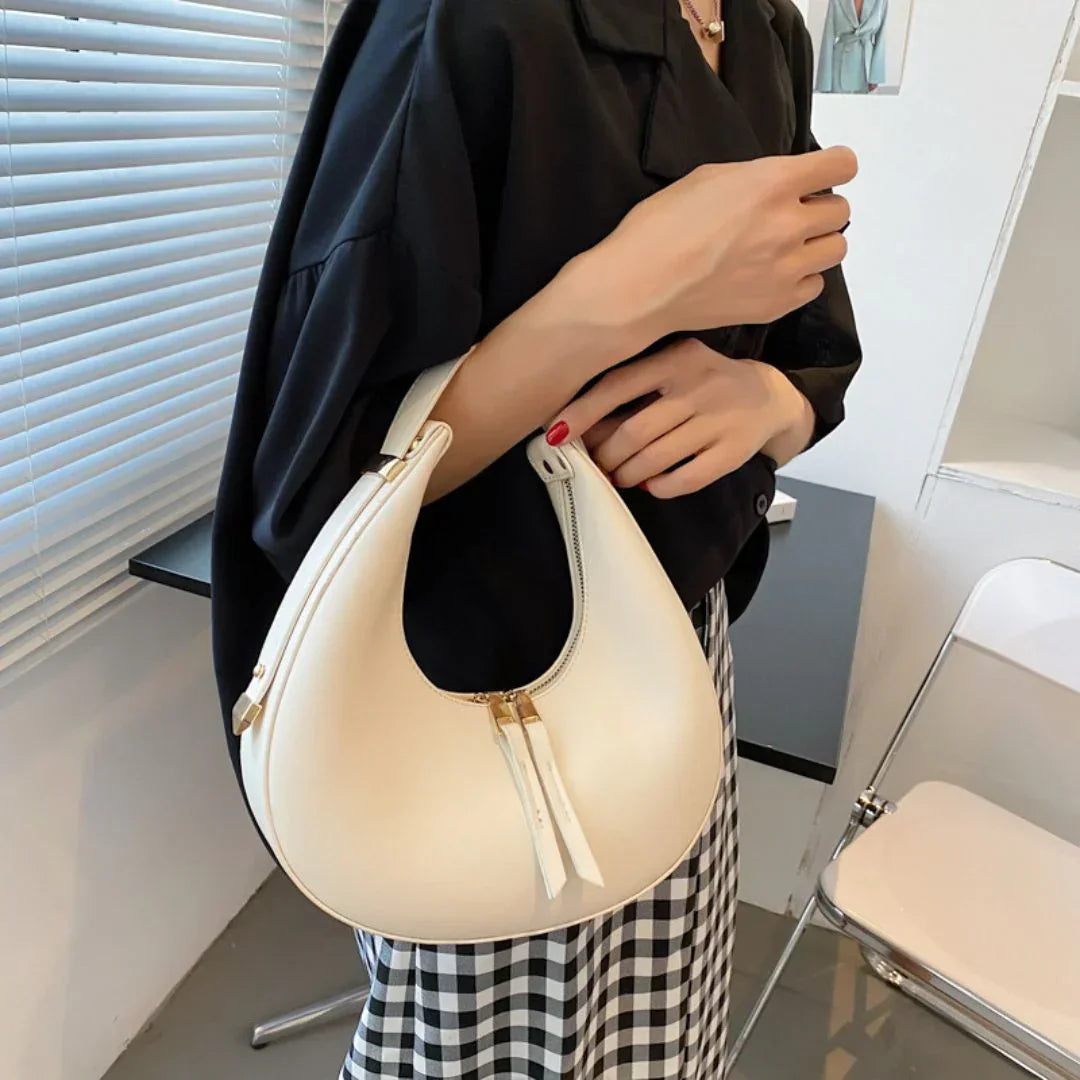 Woman holding white crescent shoulder bag, black blouse, plaid skirt, modern room