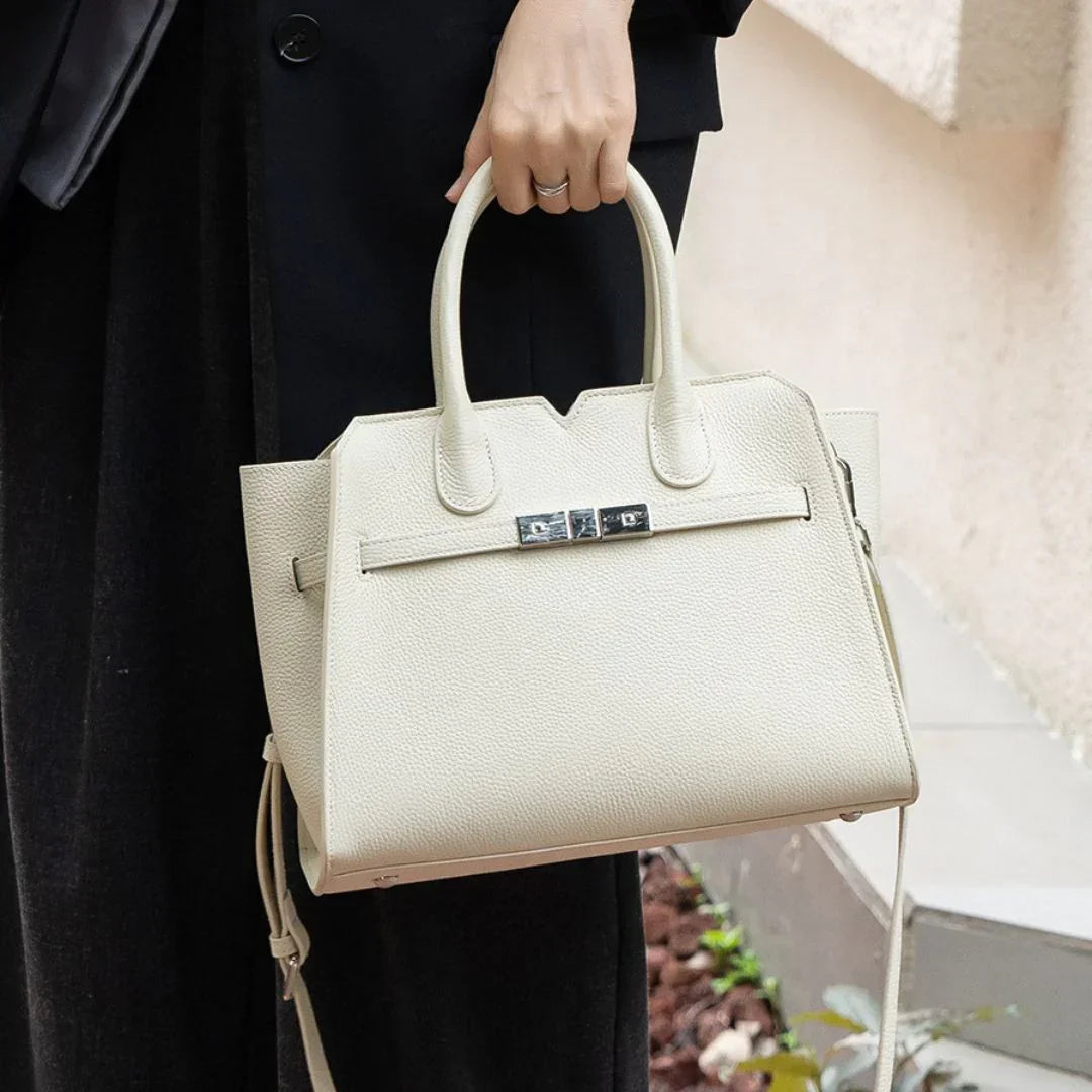 Woman holding elegant cream leather handbag with silver clasp, outdoor setting