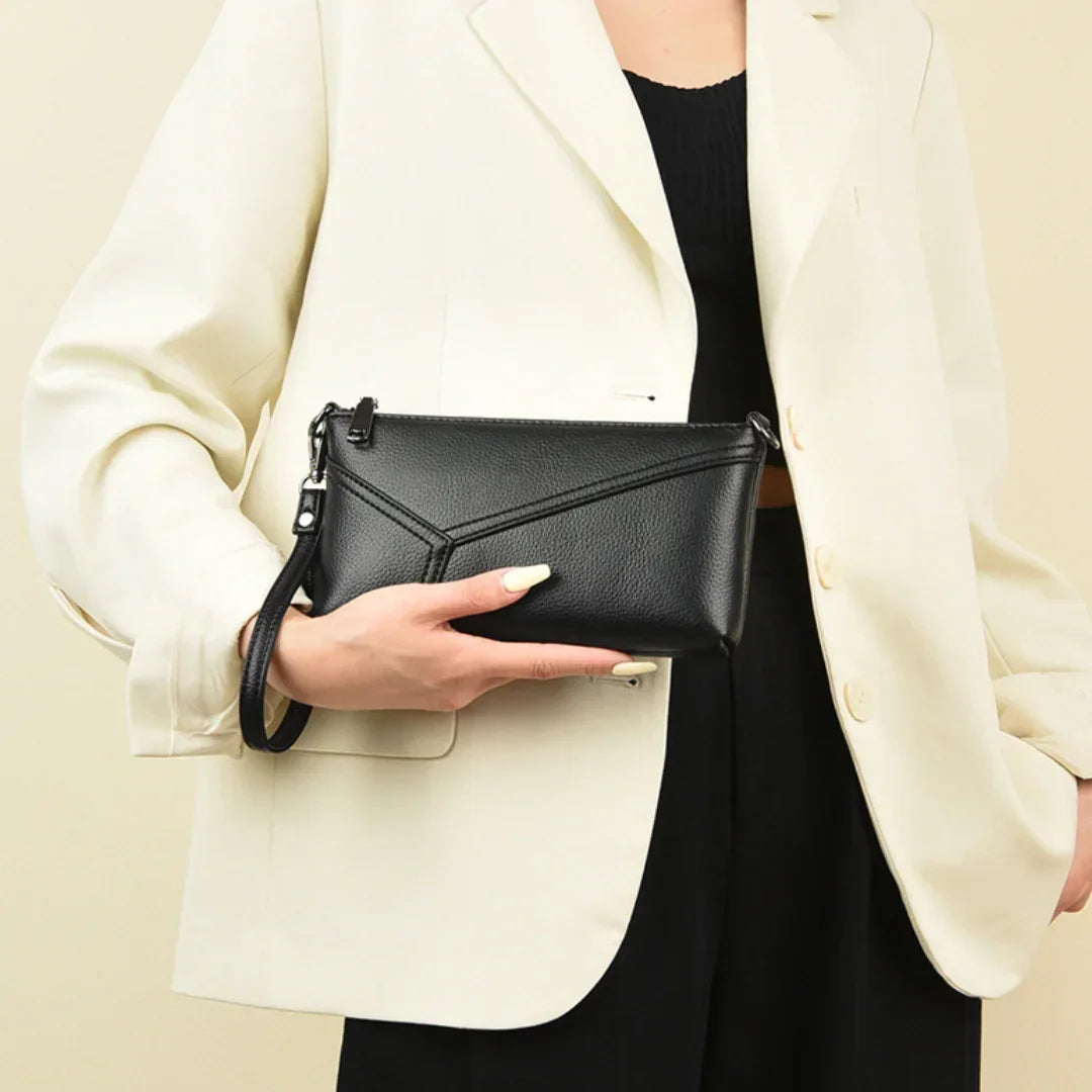 Woman in cream blazer holding black leather wristlet clutch purse