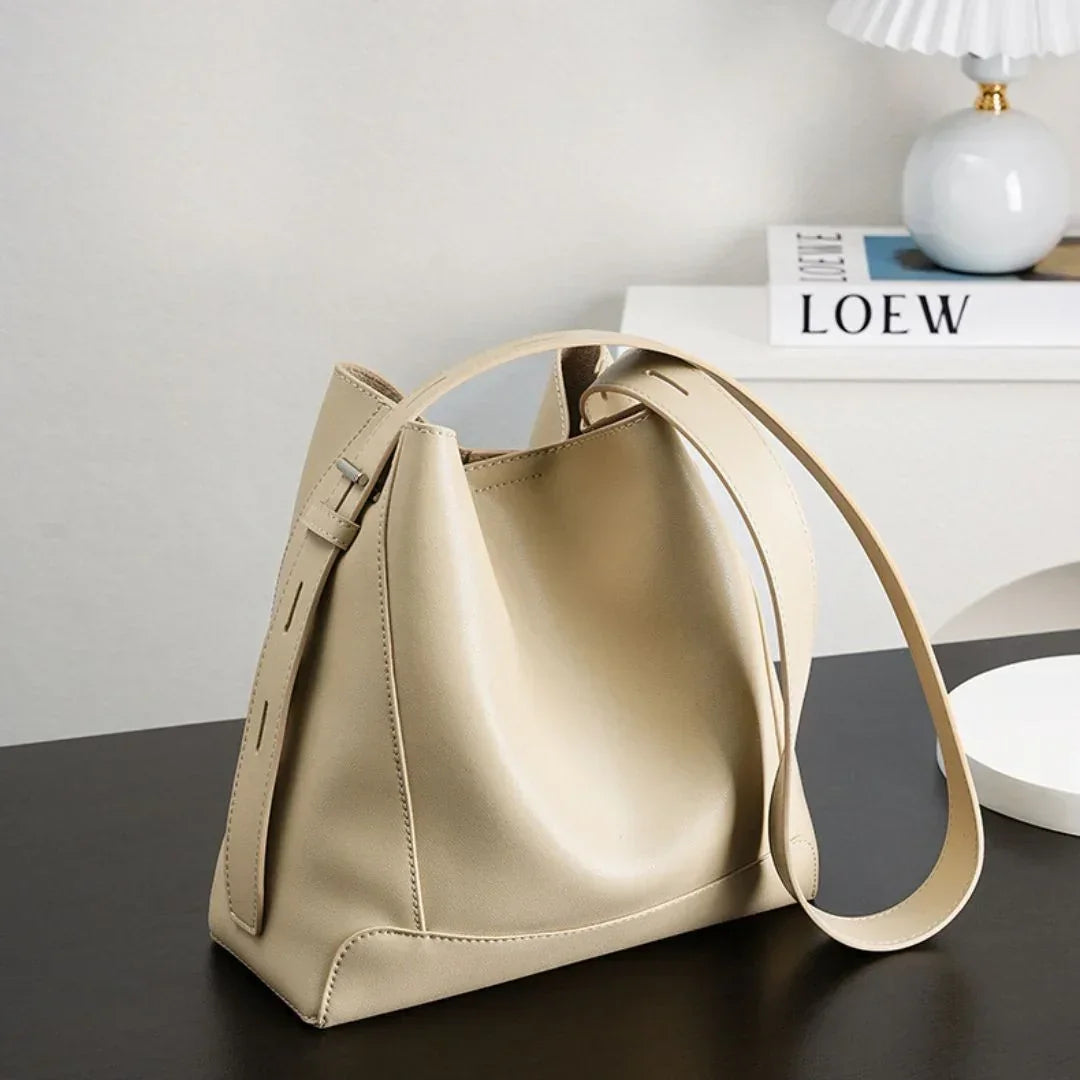Beige leather bucket bag with adjustable strap on black table, modern decor in background