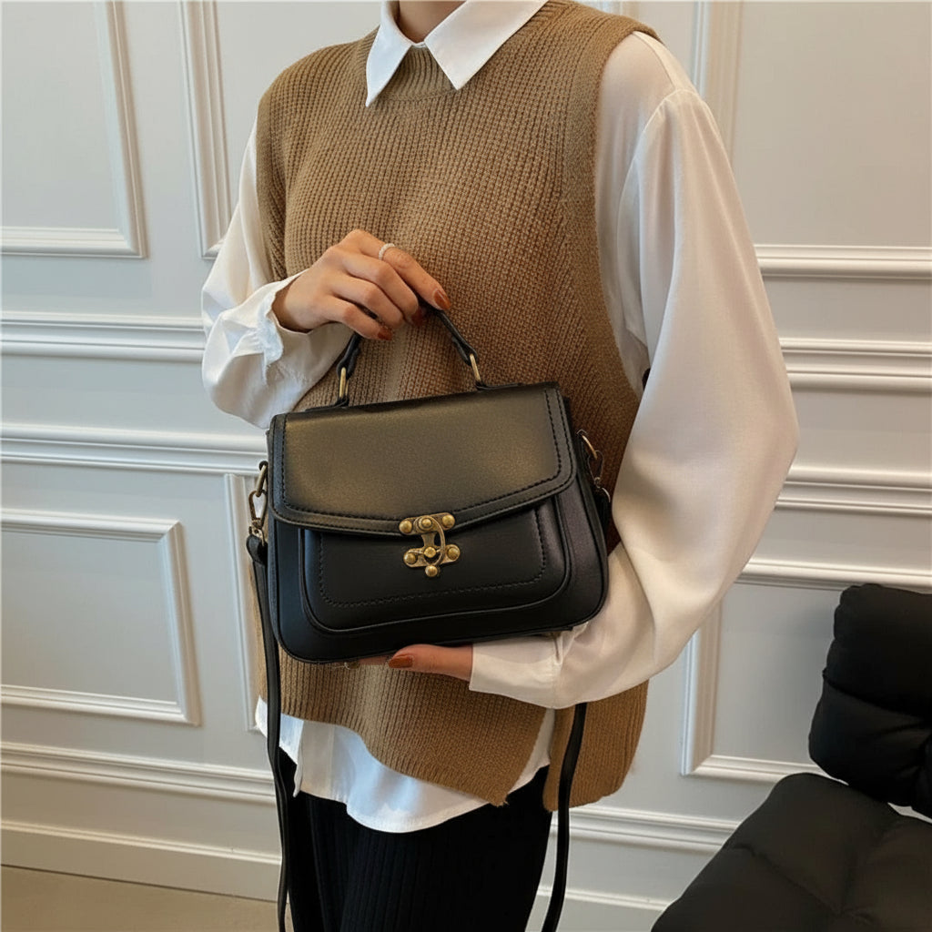 Woman holding black leather handbag with gold clasp, wearing white shirt and brown vest