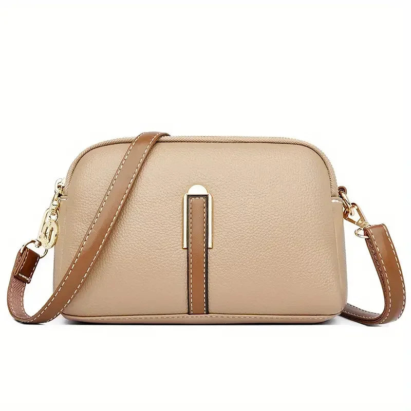 Beige leather crossbody bag with gold clasps and brown adjustable strap on white background