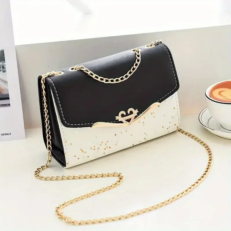 Black and white crossbody purse with gold chain strap and star pattern on white desk