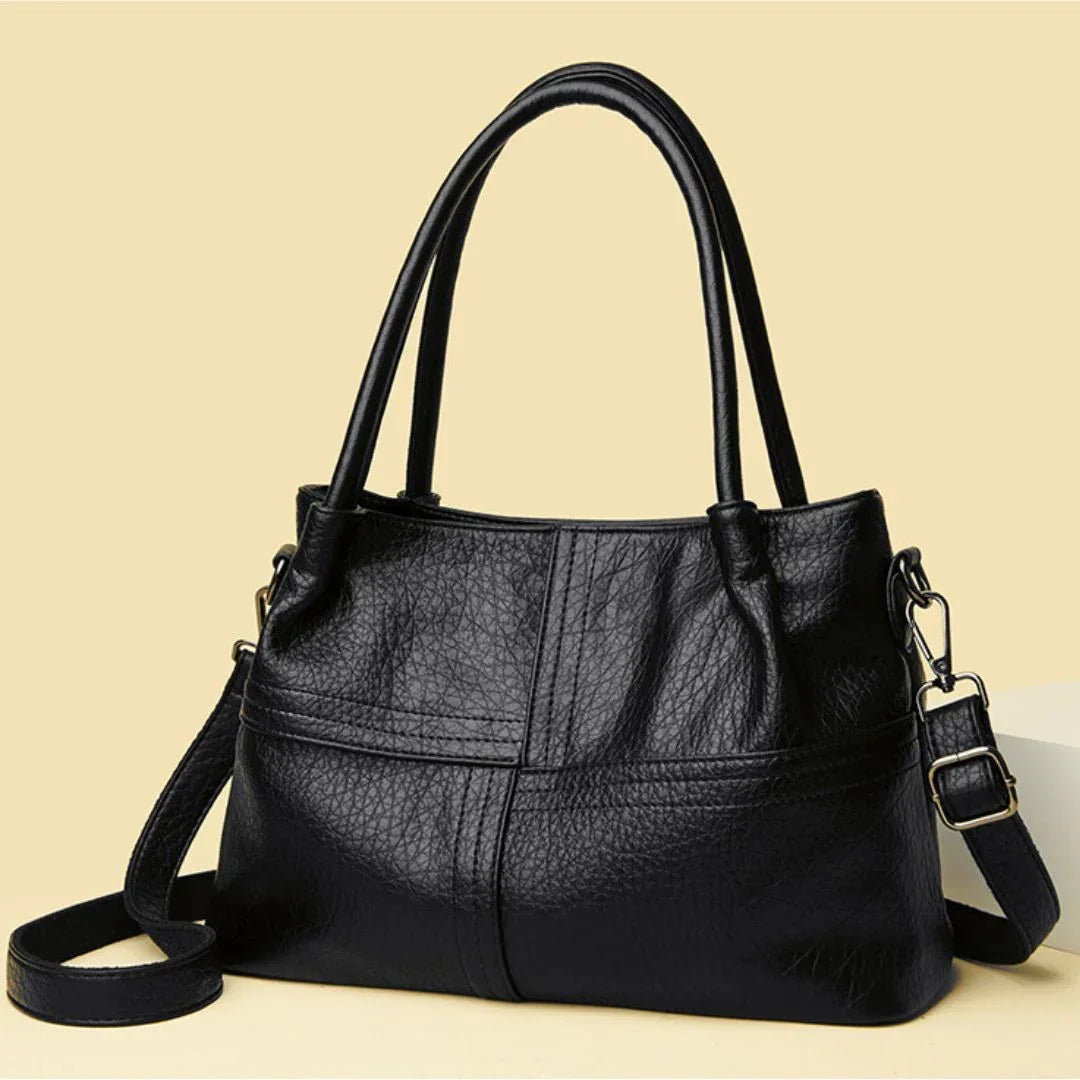 Black leather handbag with double handles and detachable shoulder strap on beige background