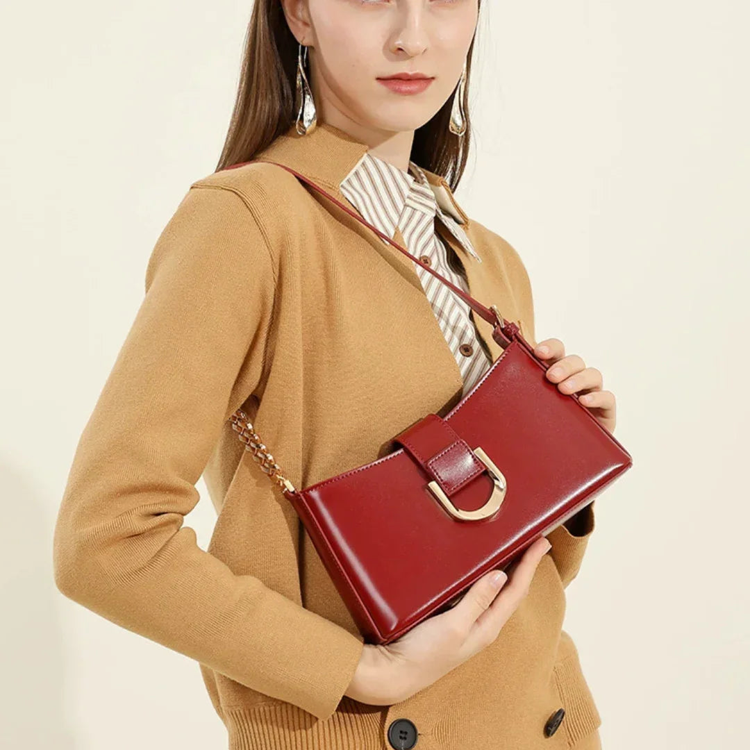 Woman in tan cardigan holding red leather shoulder bag with gold chain strap
