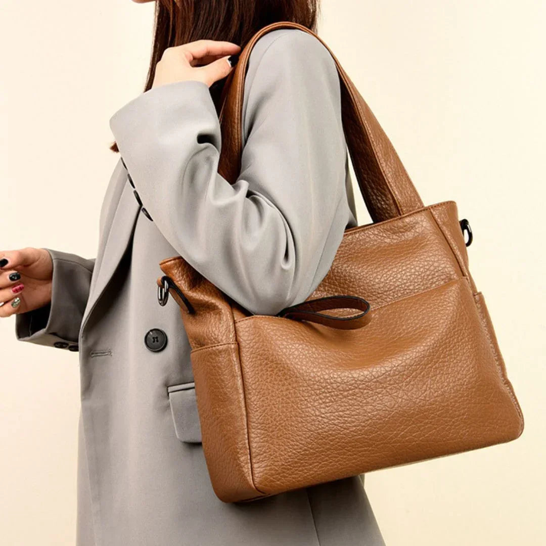 Woman in grey blazer carrying a large brown leather tote bag on shoulder