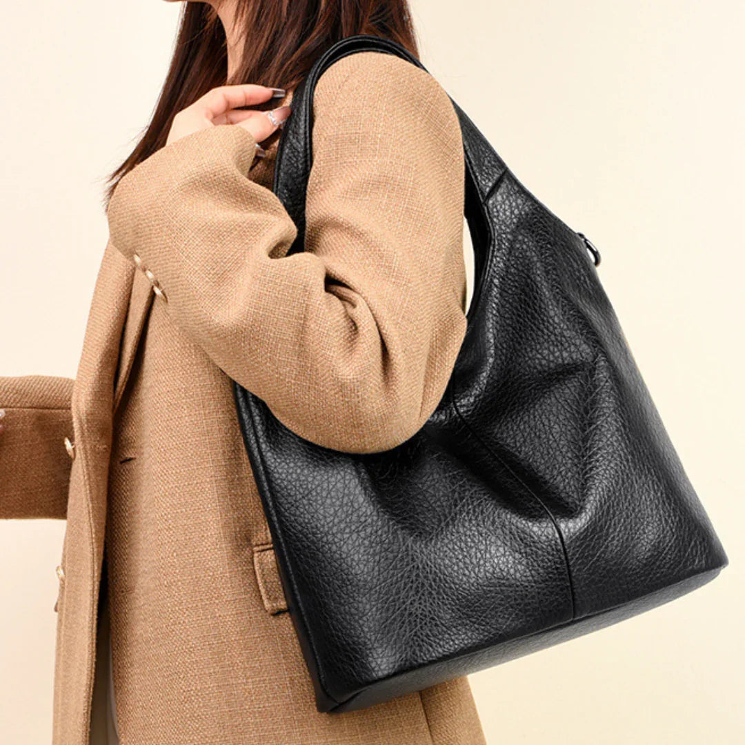 Woman wearing tan coat carrying large black leather shoulder bag