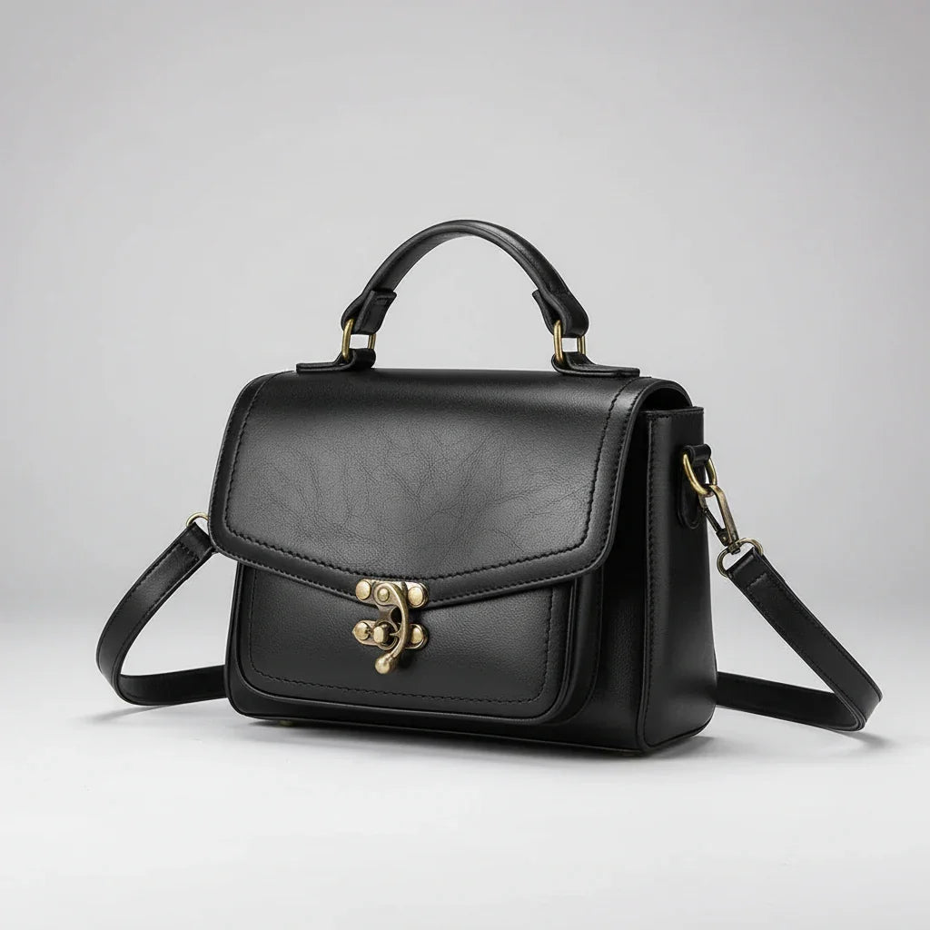Black leather handbag with gold hardware and adjustable strap on a light background