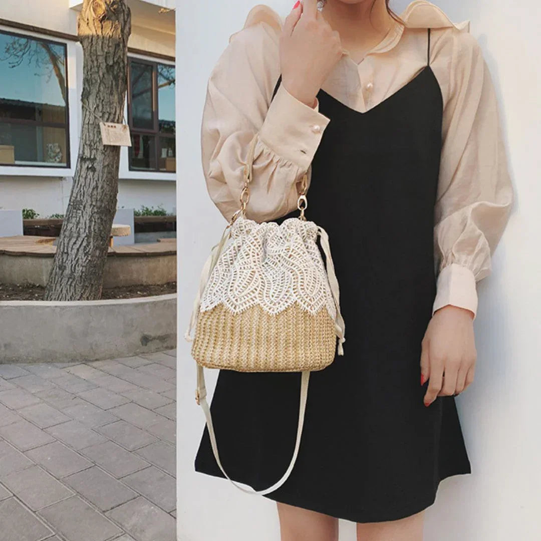 Woman in beige blouse and black dress holding a straw lace bucket bag outdoors