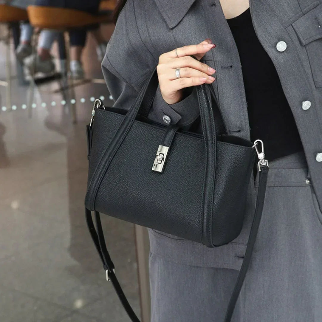 Woman in gray suit holding black leather handbag with silver clasp indoors