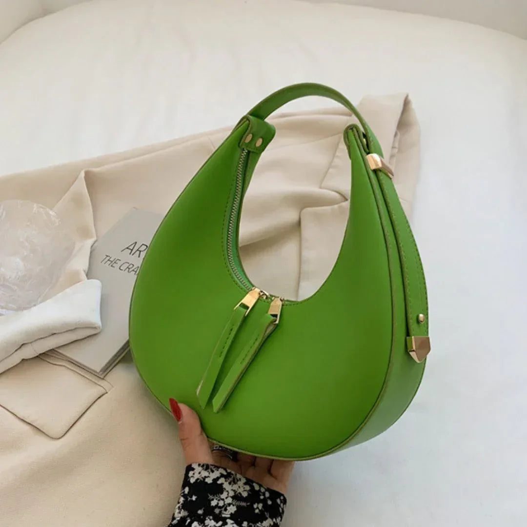 Trendy green crescent shoulder bag with gold zipper, held on beige fabric background