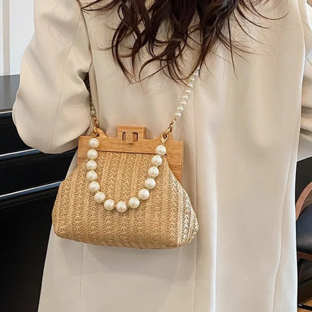Woman in beige coat carrying woven straw handbag with pearl chain strap