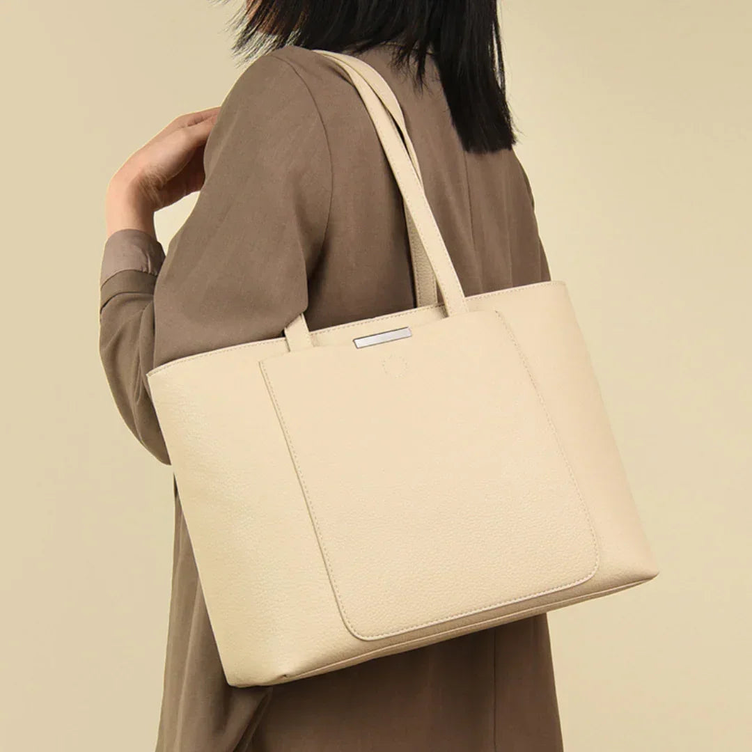 Woman carrying beige leather tote bag on shoulder against neutral background