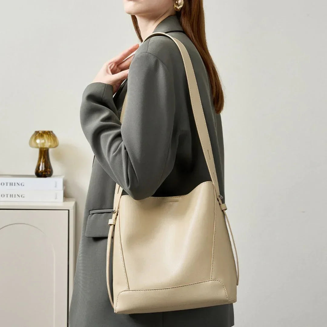 Woman in grey blazer carrying beige leather shoulder bag, minimal modern decor background