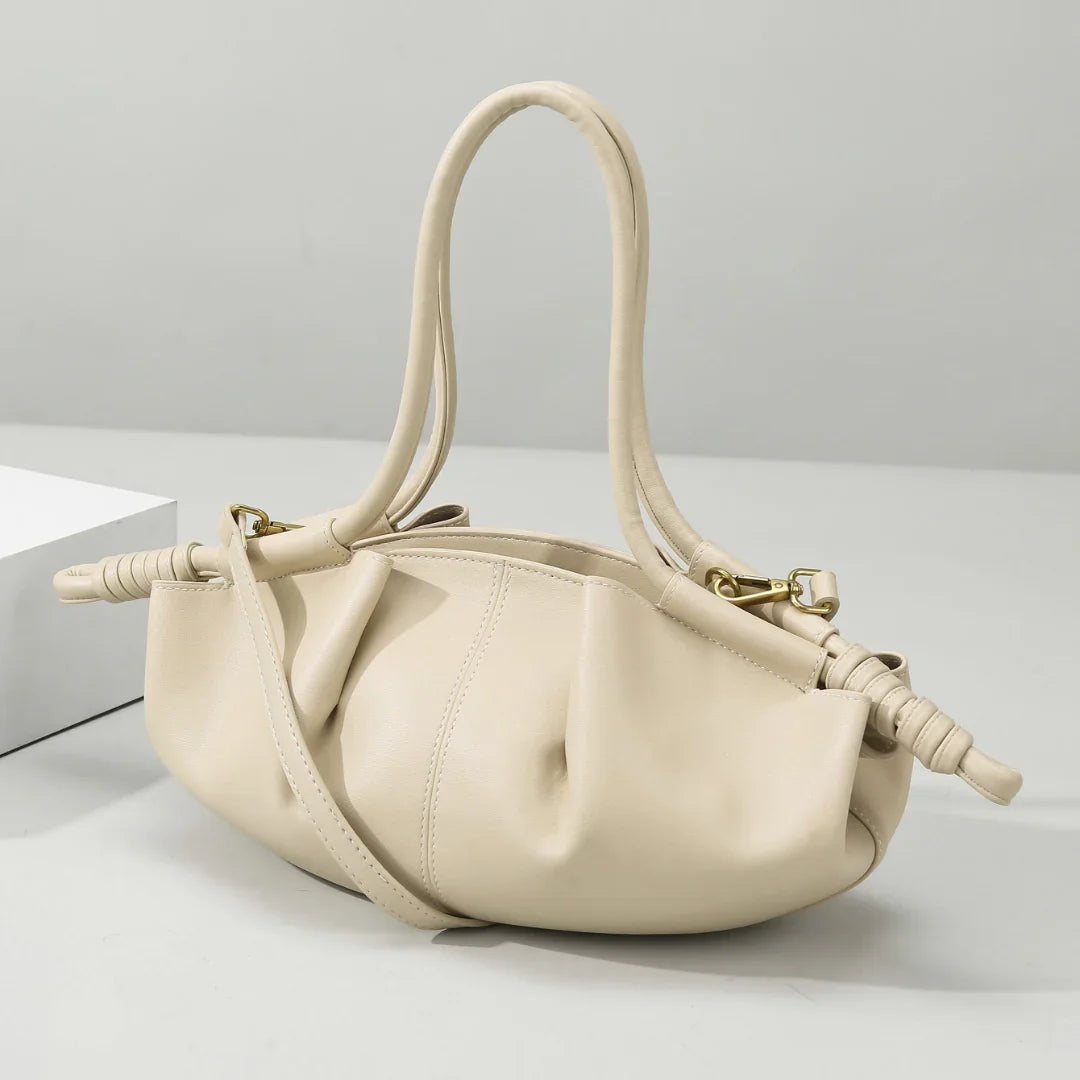 Beige leather handbag with ruched details and double handles on a white background