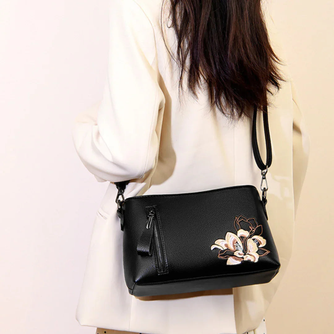 Woman in white blazer with black leather crossbody bag featuring floral embroidery