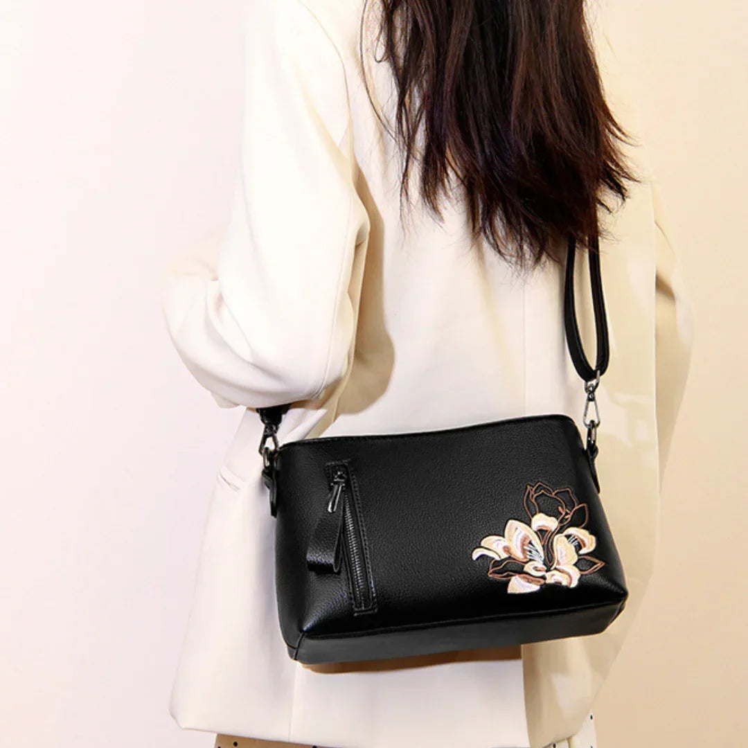 Woman in white blazer with black leather crossbody bag featuring floral embroidery