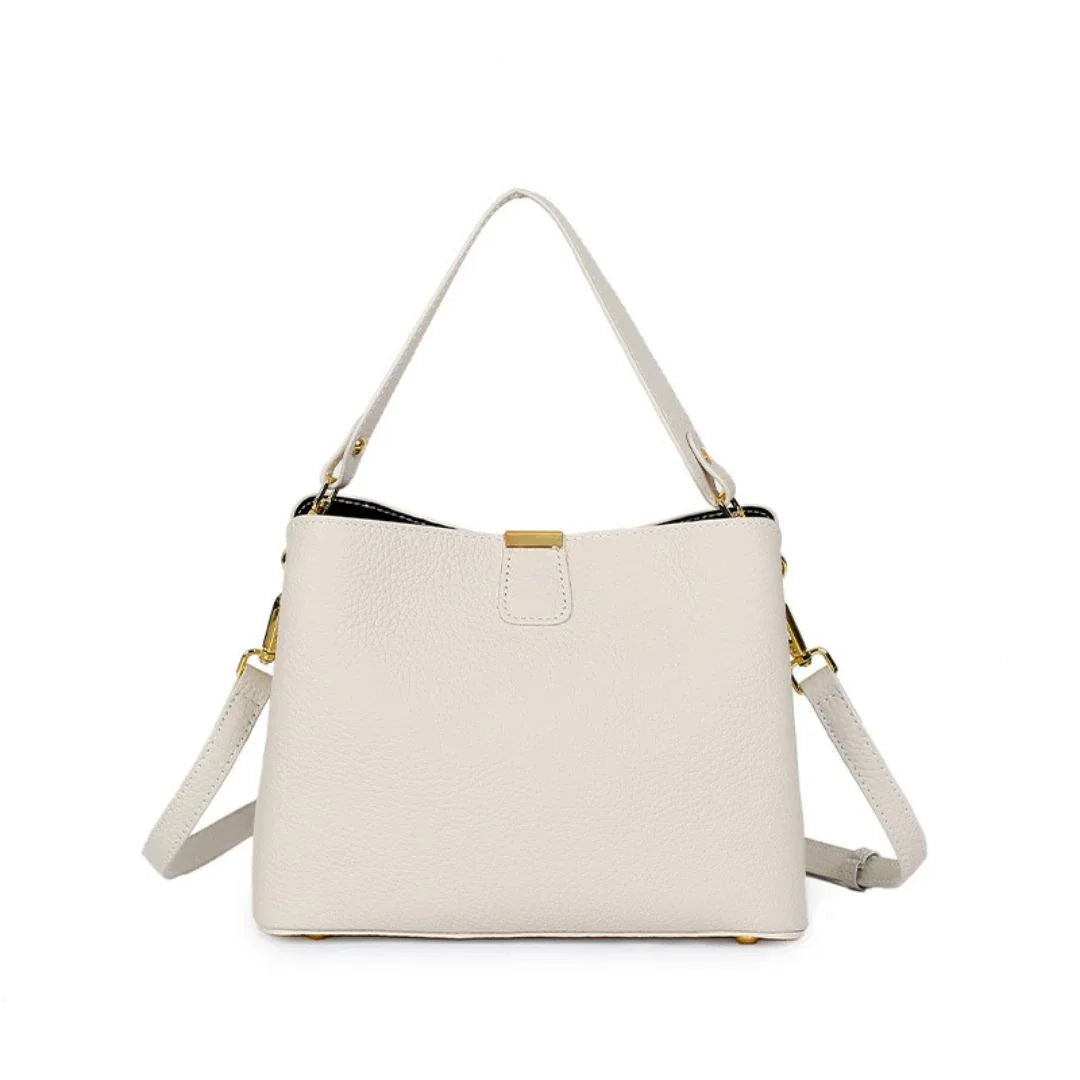 Ivory leather handbag with gold hardware and adjustable shoulder strap on white background