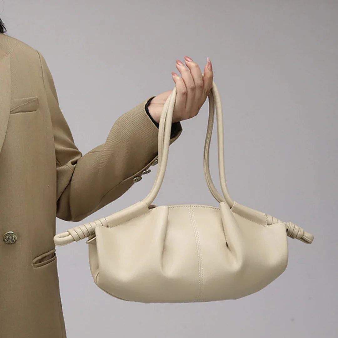 Woman in beige blazer holding cream leather handbag with knotted handles