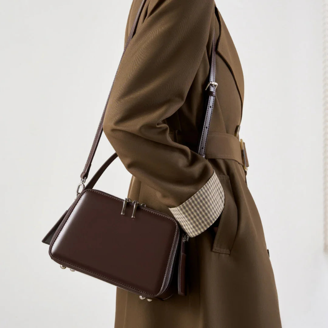 Brown leather crossbody bag styled with a tan trench coat, fashion accessory detail