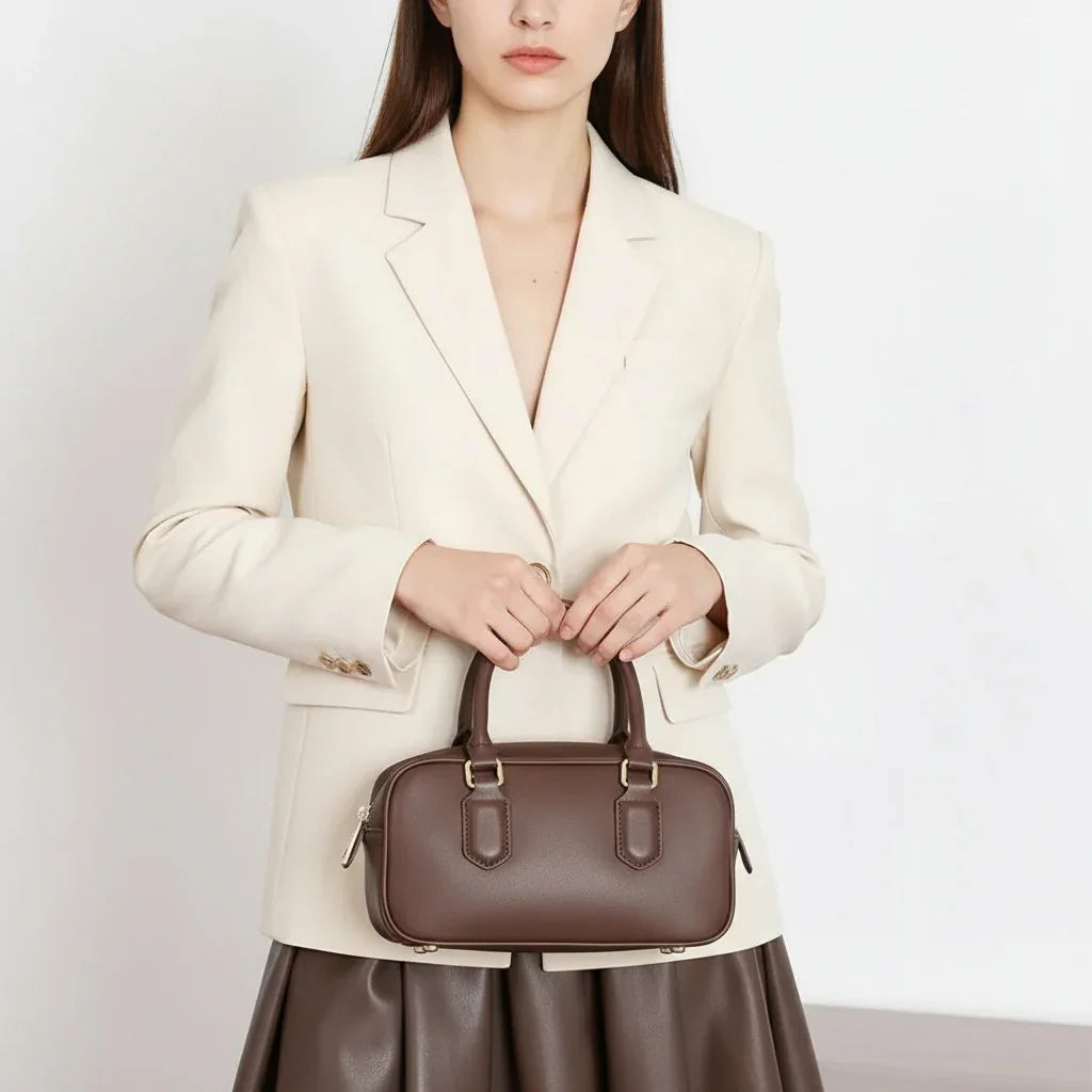 Woman in cream blazer holding brown leather handbag, fashion accessory product photo