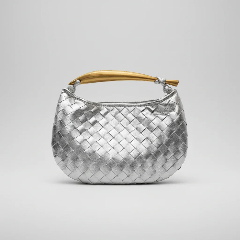 Silver woven leather handbag with gold curved handle on plain light background