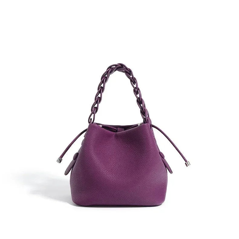 Purple leather bucket bag with braided handle and drawstring closure on white background