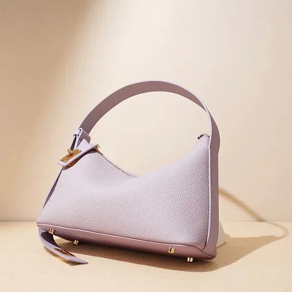 Lavender textured leather shoulder bag with gold hardware on beige background