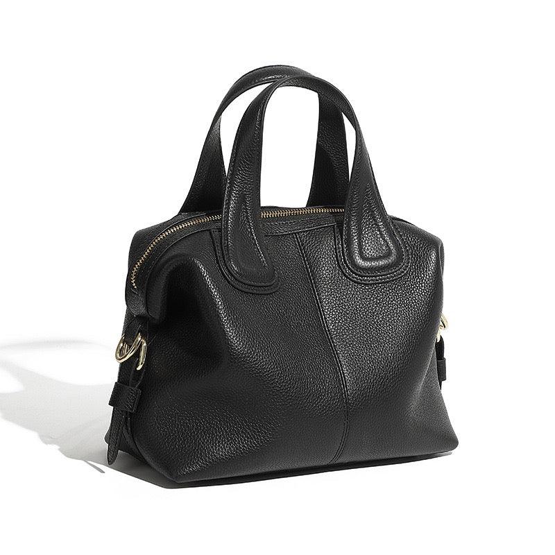 Black leather handbag with gold zipper and dual handles on white background
