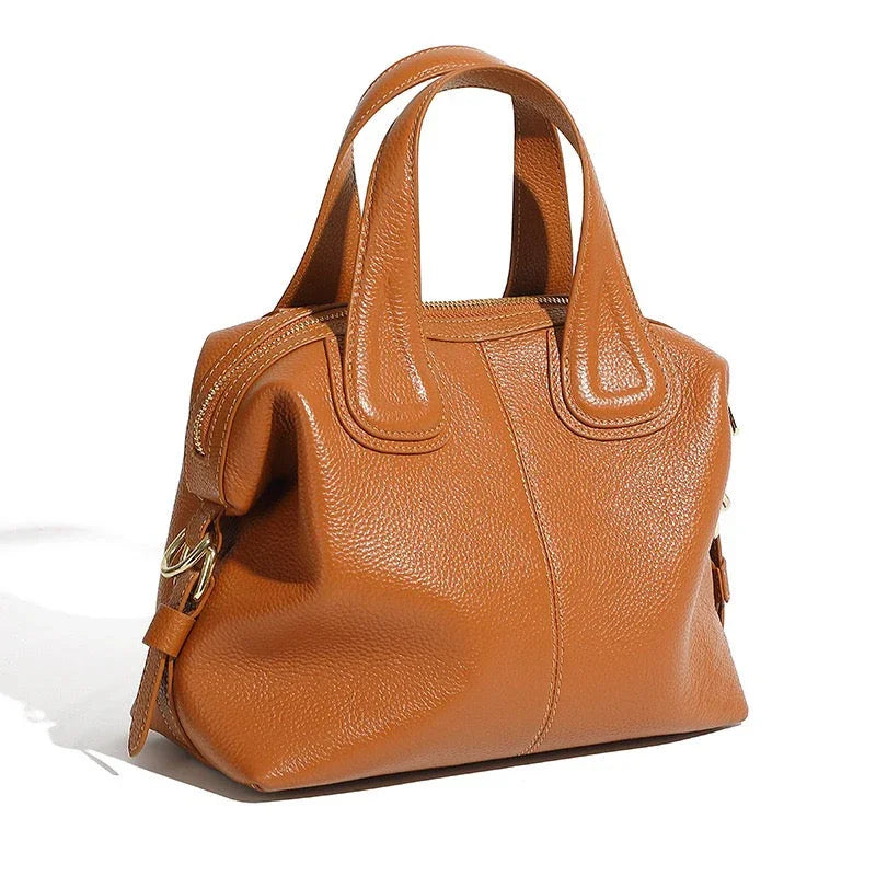 Brown leather handbag with gold hardware and short handles on a white background