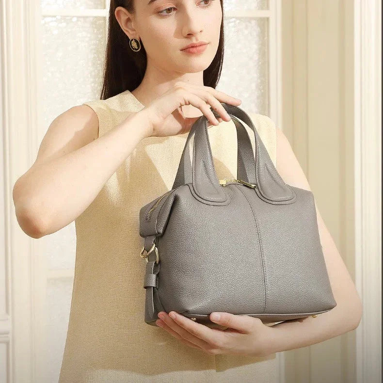 Woman holding a stylish gray leather handbag indoors, fashion accessory display