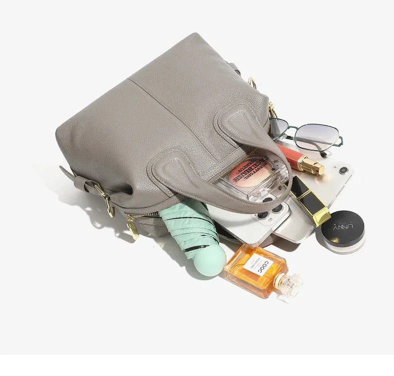 Gray leather handbag with makeup, perfume, glasses, tablet, and wallet spilling out