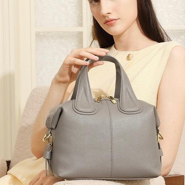 Woman holding a gray leather handbag with gold hardware sitting on a cream chair
