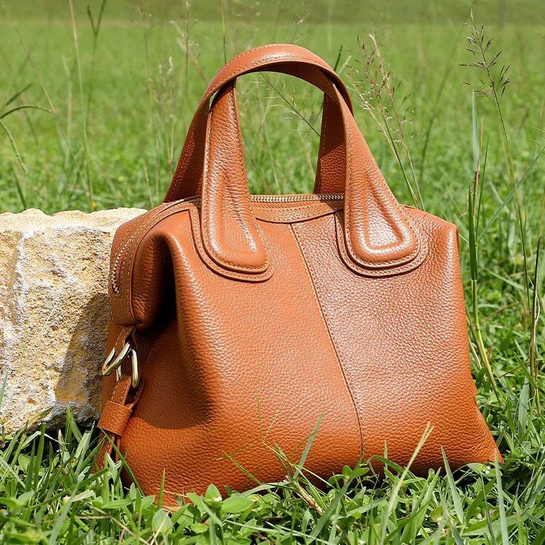 Brown leather handbag on grass beside stone, luxury purse outdoor product photo