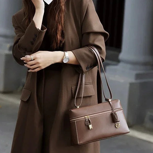 Woman in brown coat holding a brown leather handbag with gold hardware outdoors