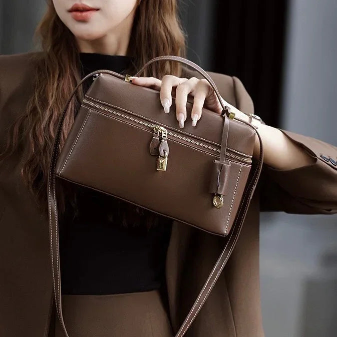 Woman in brown suit holding a brown leather crossbody handbag with gold hardware