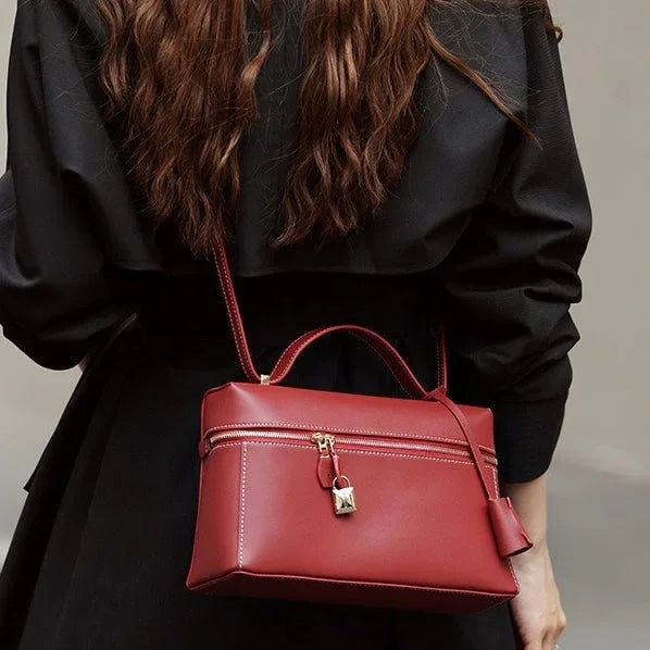 Woman in black outfit carrying a red leather crossbody handbag with lock detail