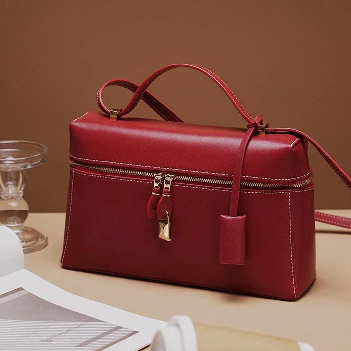 Elegant red leather handbag with gold zipper on beige table, minimal background