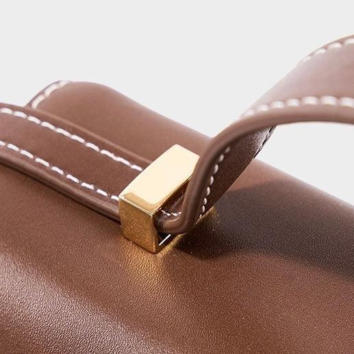 Brown leather handbag handle with white stitching and gold hardware detail