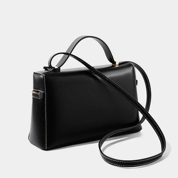 Black leather handbag with top handle and long shoulder strap on white background