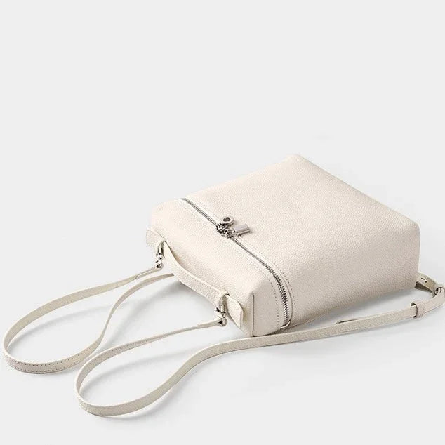 Minimalist white leather crossbody bag with zipper and adjustable strap on light background
