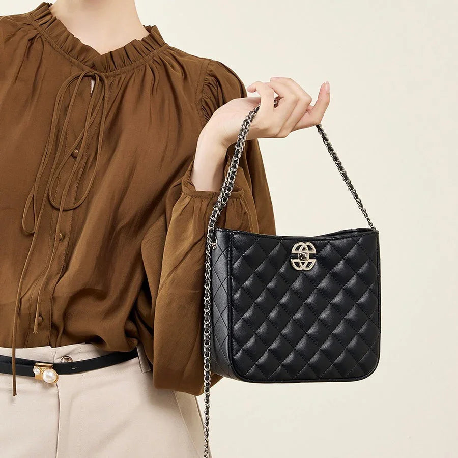 Woman holding black quilted leather shoulder bag with chain strap and gold logo, brown blouse