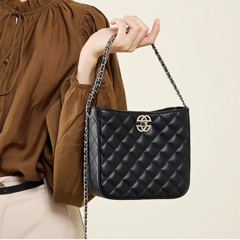 Woman holding black quilted leather shoulder bag with chain strap and gold logo