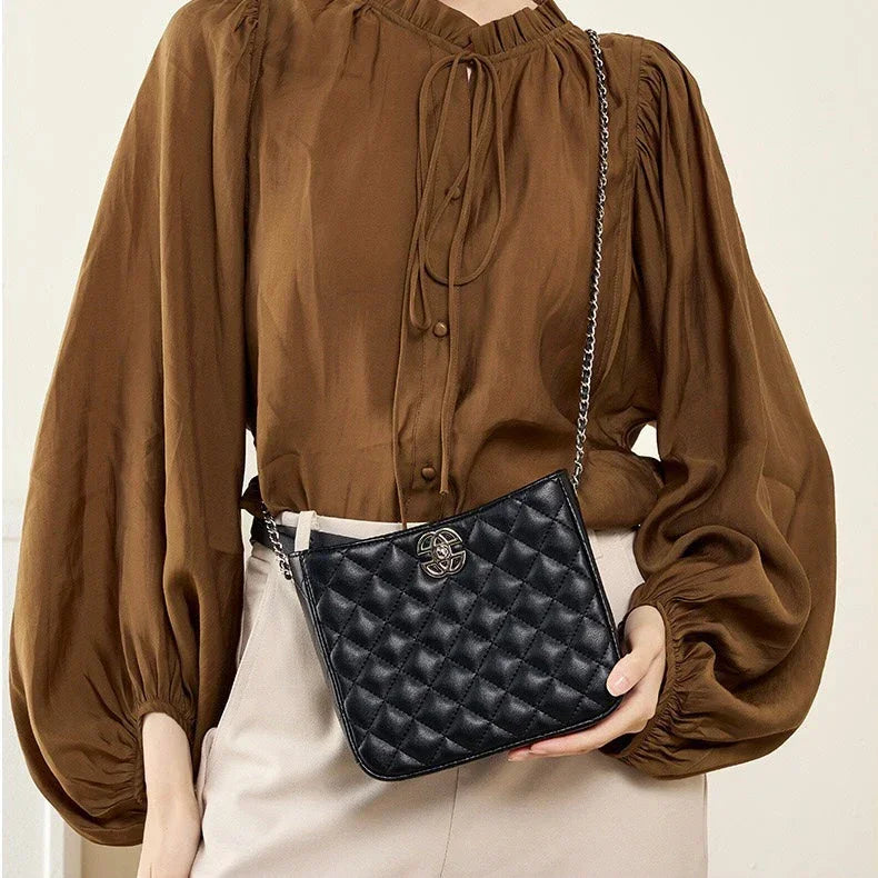 Woman in brown blouse and beige pants holding black quilted crossbody bag